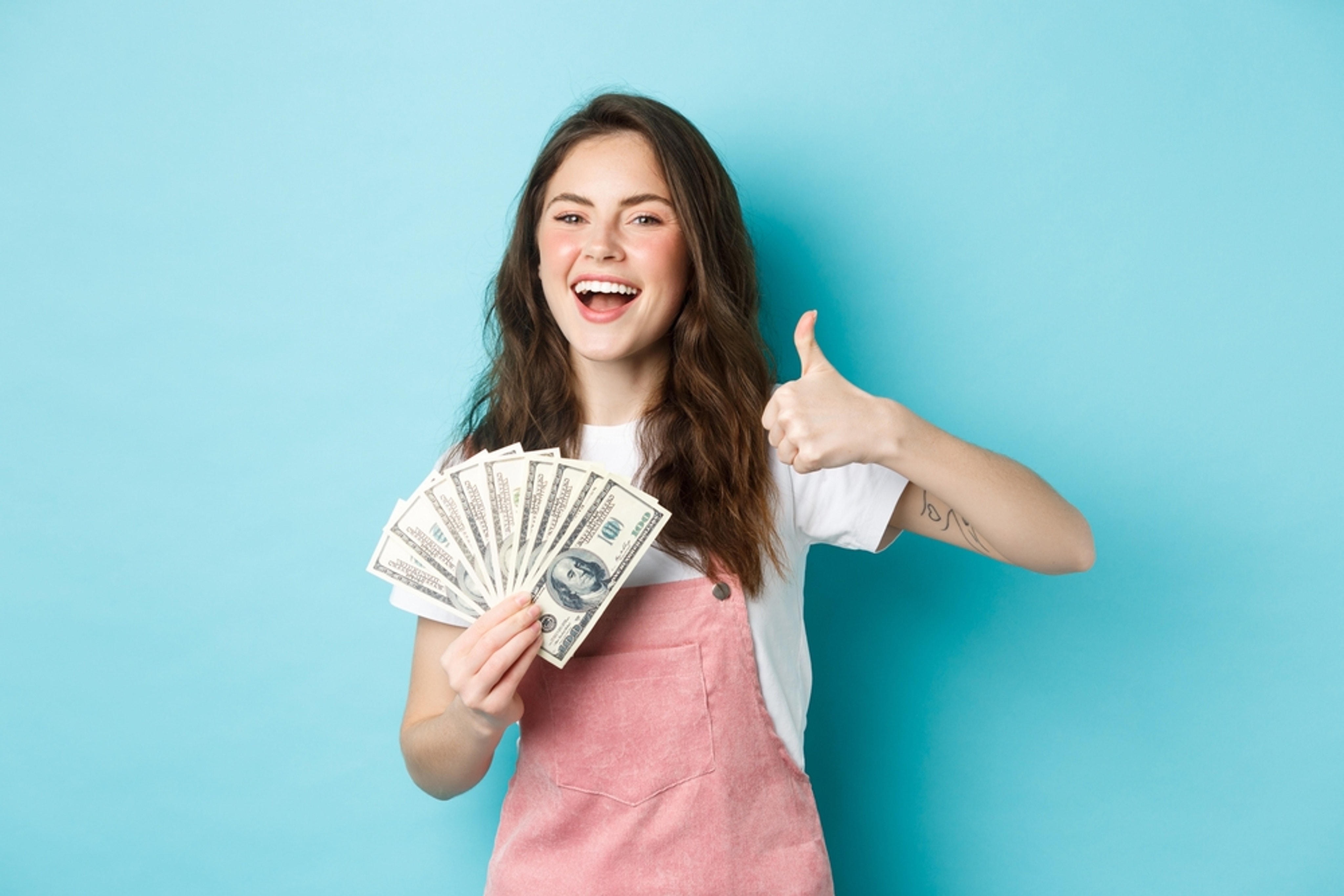 Smiling,Happy,Woman,Holding,Money,,Dollar,Bills,And,Showing,Thumb